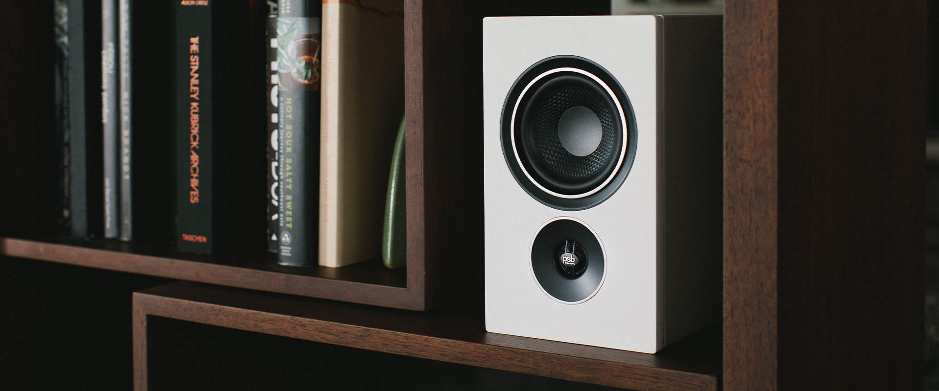 Close up on one of two Alpha iQ Streaming Powered Speakers on a stylish modern wood book filled bookshelf.